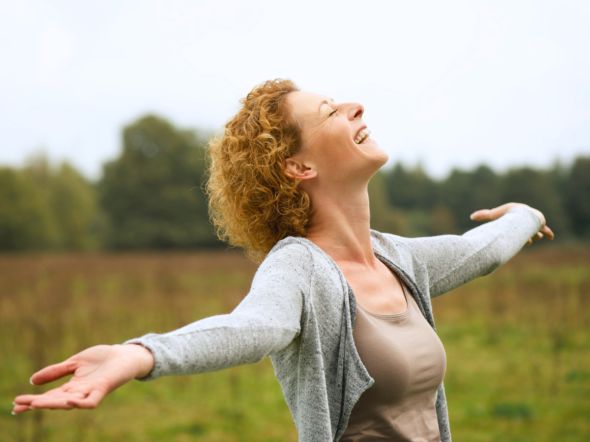 Mujer sonriendo ampliamente con brazos extendidos en la naturaleza